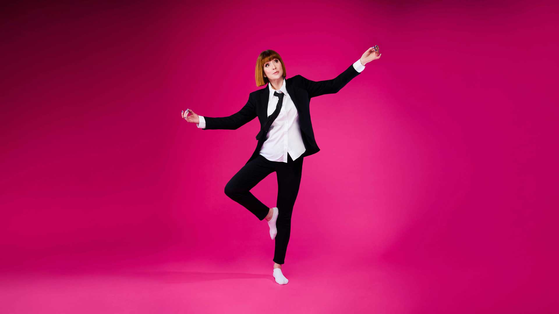 Cally Beaton wears a suit and balances on one leg in a yoga pose.