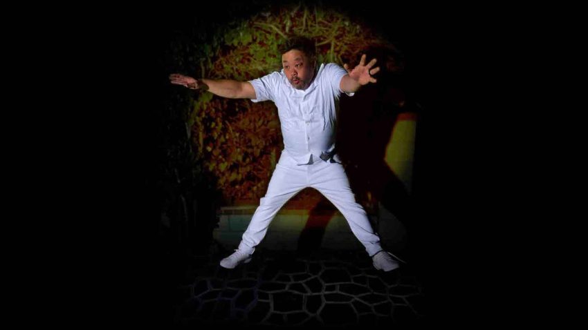 A man dressed in white jumps in the air with his limbs outstretched.