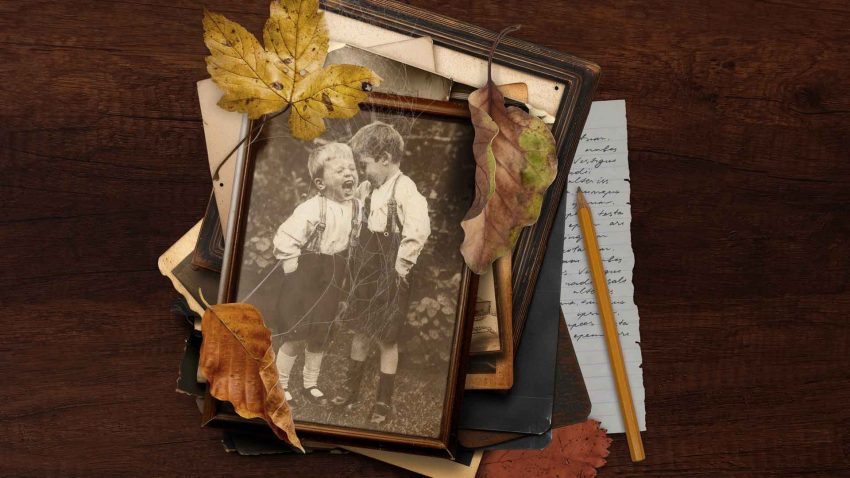A photo frame shows two young boys laughing. Surrounding the frame are leaves, and bits of paper.