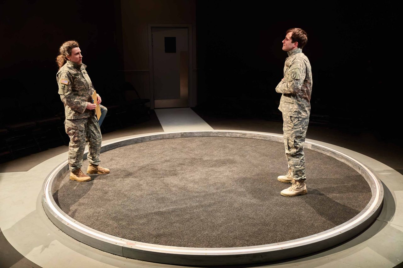 Two people standing on a circular carpet wearing army clothing, production shot from 9 Circles at the Park Theatre By Bill Cain