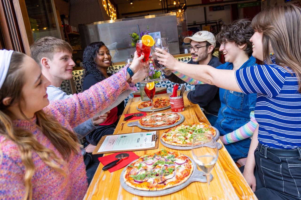 Photo of people smiling and enjoying pizza and drinks, celebrating and having a cheers moment