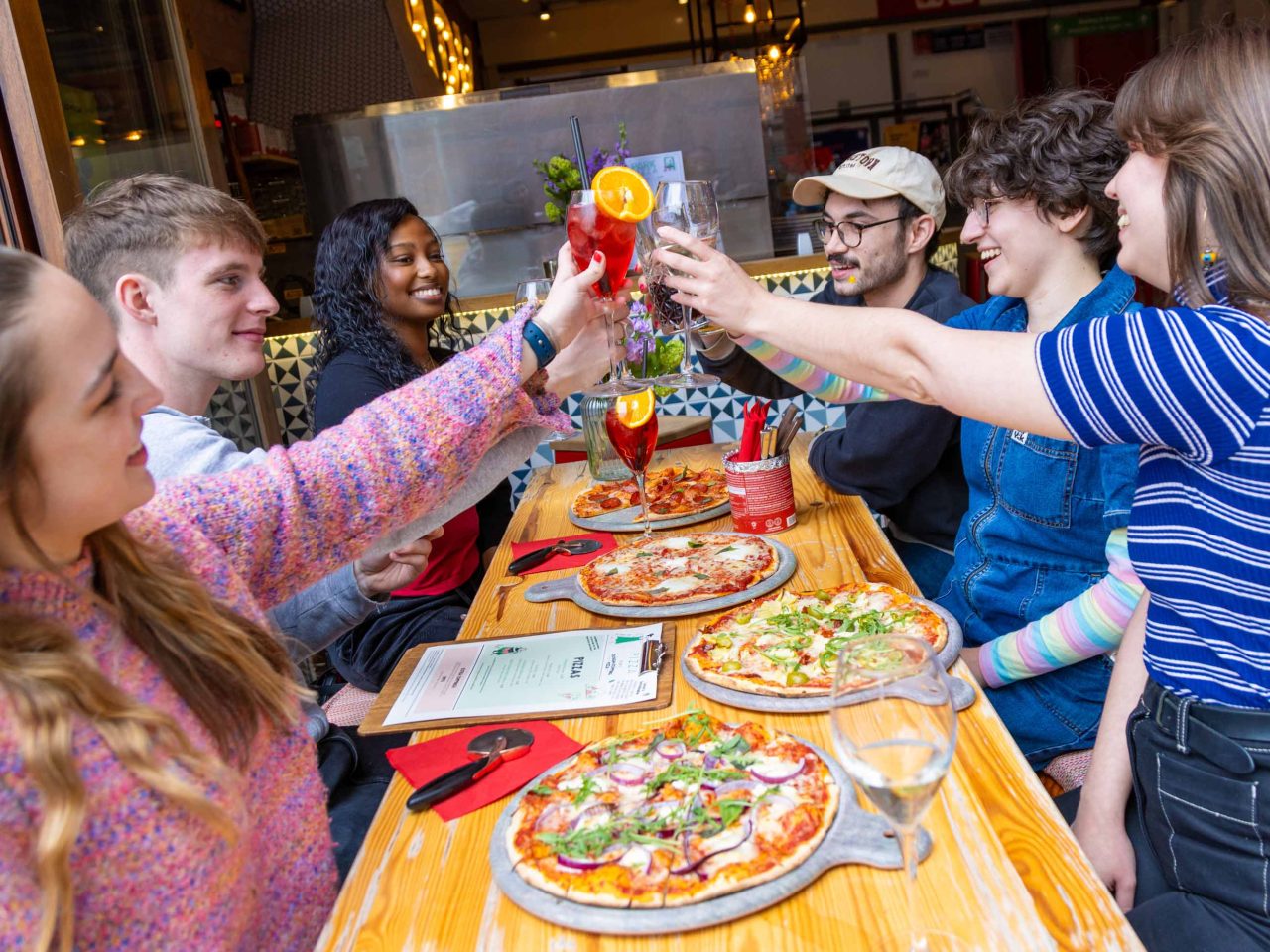 Photo of people smiling and enjoying pizza and drinks, celebrating and having a cheers moment