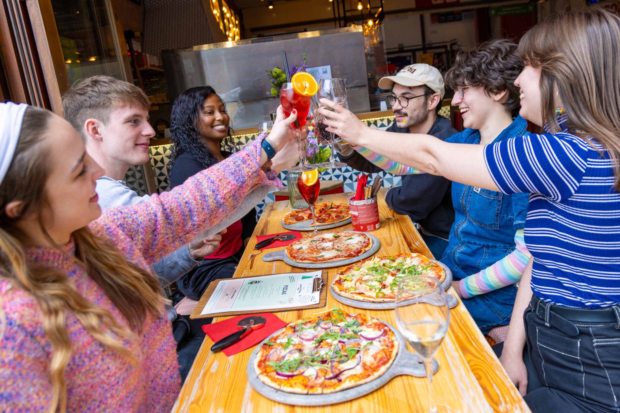 Photo of people smiling and enjoying pizza and drinks, celebrating and having a cheers moment