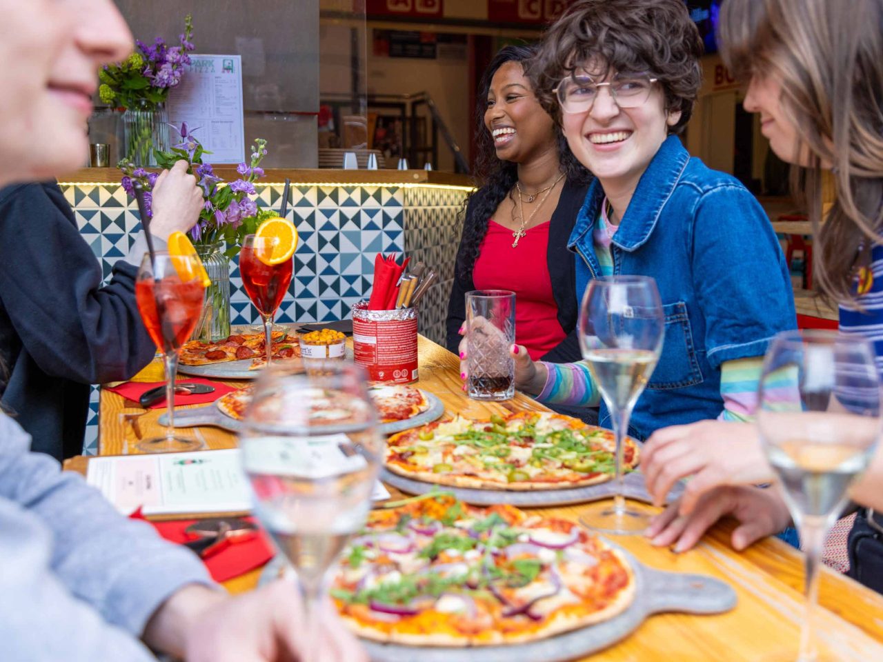 Photo of people enjoying pizza and drinks laughing and chatting
