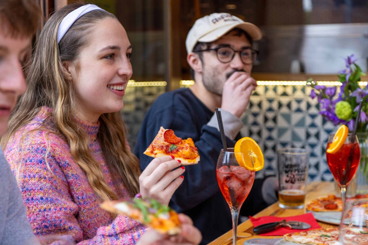 Photo of people enjoying pizza and drinks, 2 friends chatting and enjoying an evening out