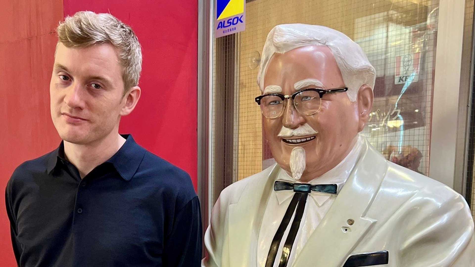 A photo of comedian James Acaster standing next to Colonel Sanders